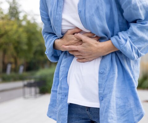 Jemand steht draußen und hält sich den Bauch.