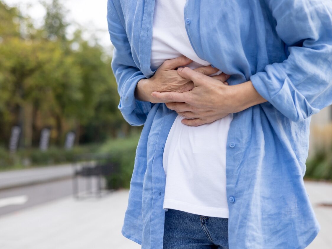 Jemand steht draußen und hält sich den Bauch.