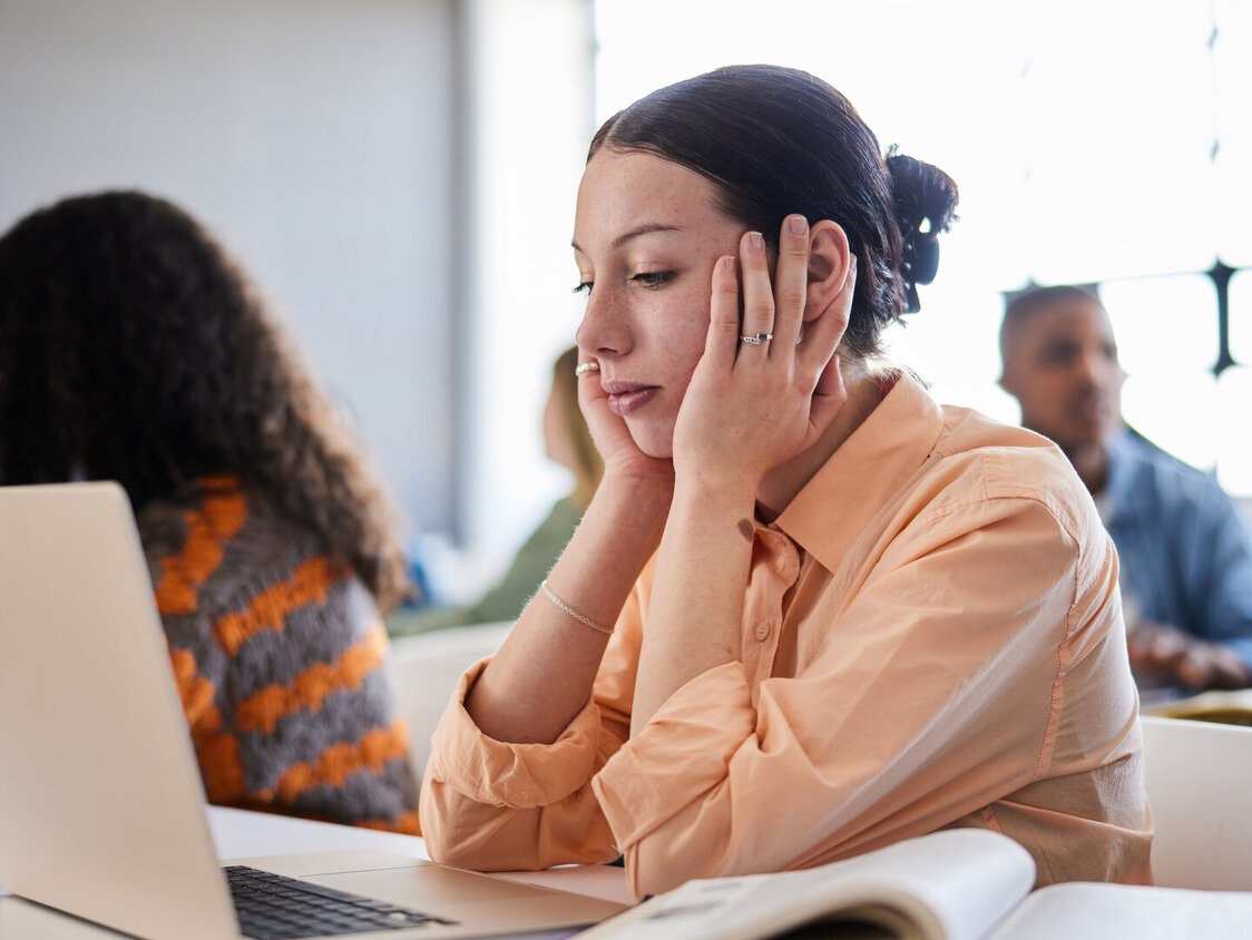 Junge Frau sitzt am Schreibtisch und hält sich den Kopf