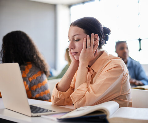 Junge Frau sitzt am Schreibtisch und hält sich den Kopf