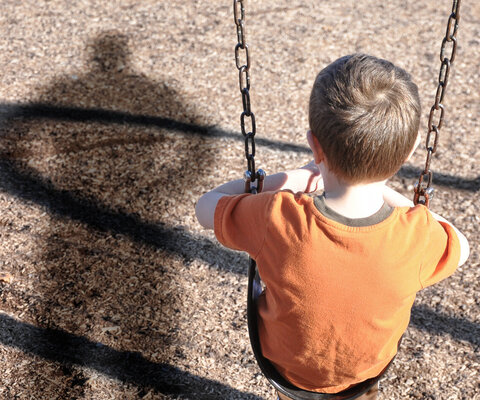 trauriges Kind auf der Schaukel mit Schatten eines Erwachsenen