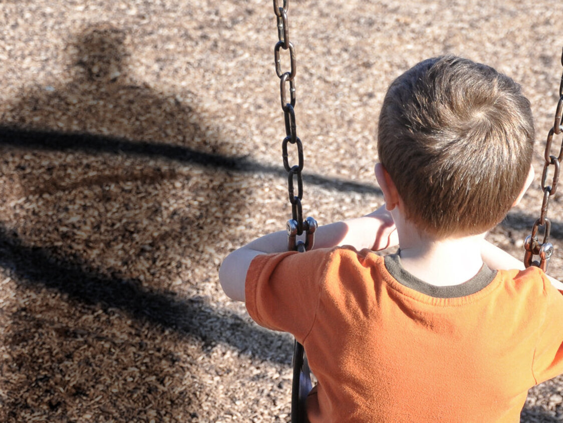 trauriges Kind auf der Schaukel mit Schatten eines Erwachsenen