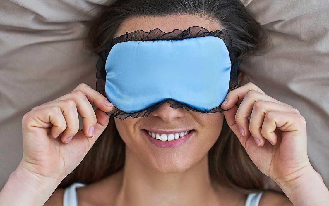 Eine lächelnde Frau mit blauer Schlafmaske.