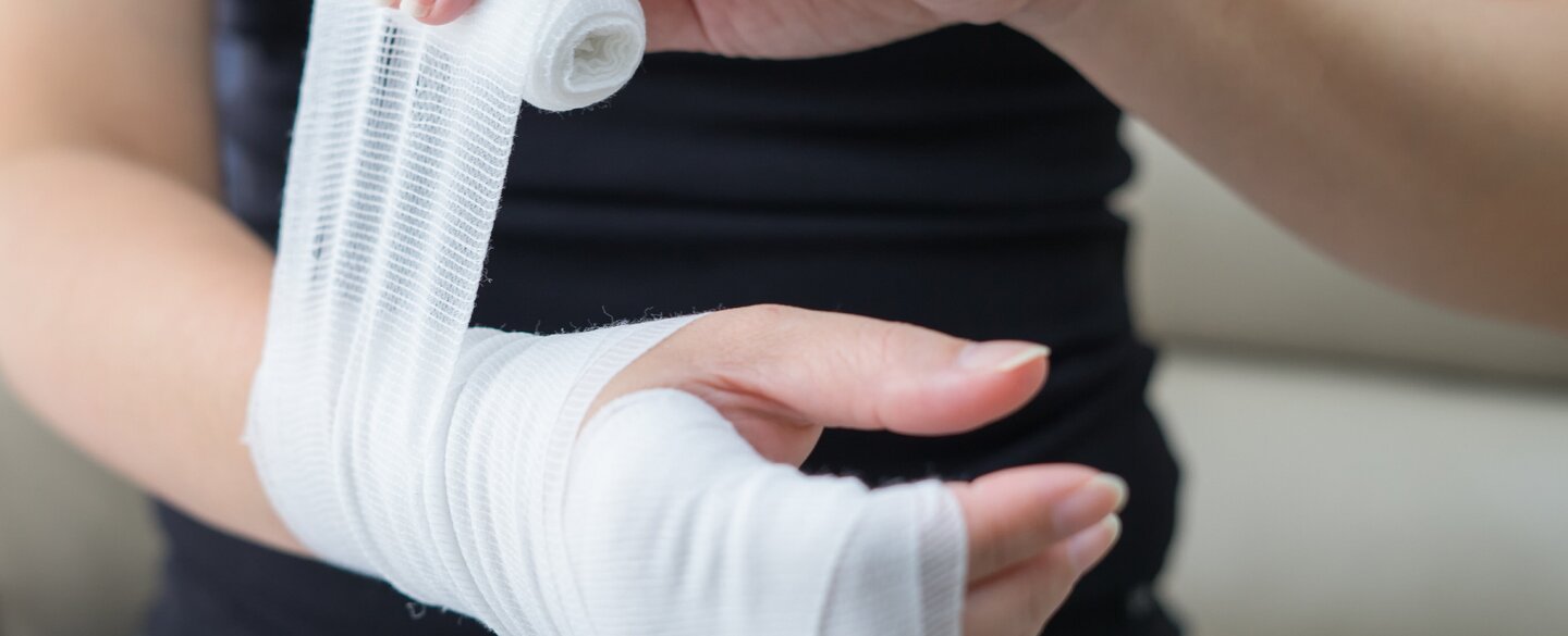 Eine Frau wickelt ihre Hand und Arm in einen Verband ein.