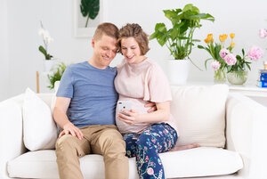 Ein Mann sitzt mit einer schwangeren Frau auf einem Sofa.
