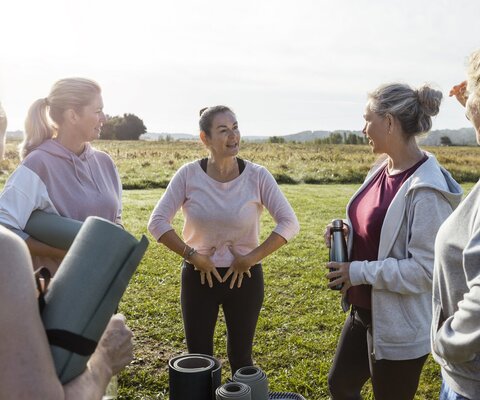 Eine Gruppe von Frauen steht draußen und eine Frau zeigt auf ihren Beckenboden.