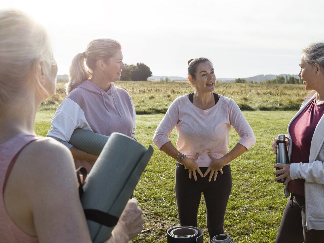 Eine Gruppe von Frauen steht draußen und eine Frau zeigt auf ihren Beckenboden.