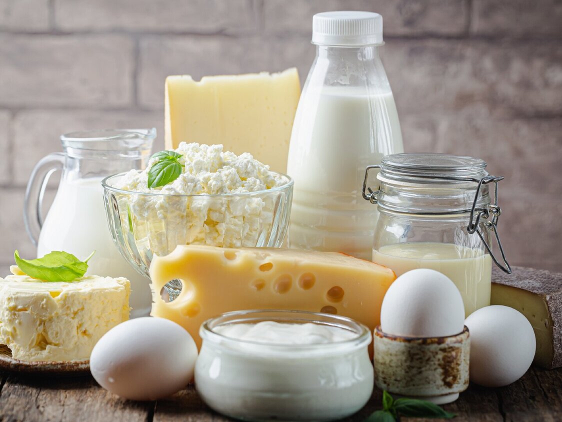 Milch, Eier und Käse stehen auf einem Holztisch.