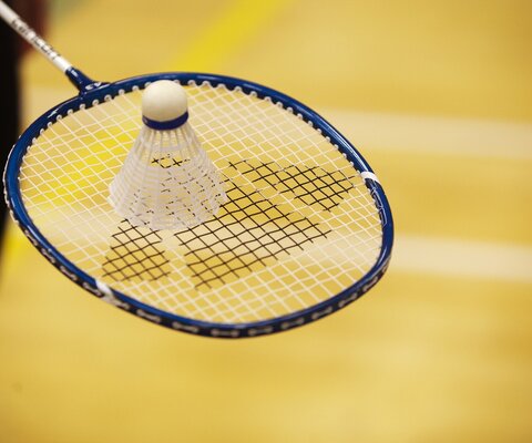 Ein Federball liegt auf einem Federballschläger. Der Hintergrund ist gelb.