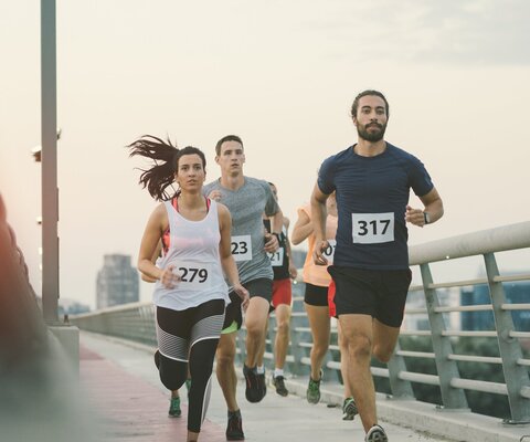 Mehrere Personen mit Startnummern auf ihren Shirts laufen auf einer Brücke.