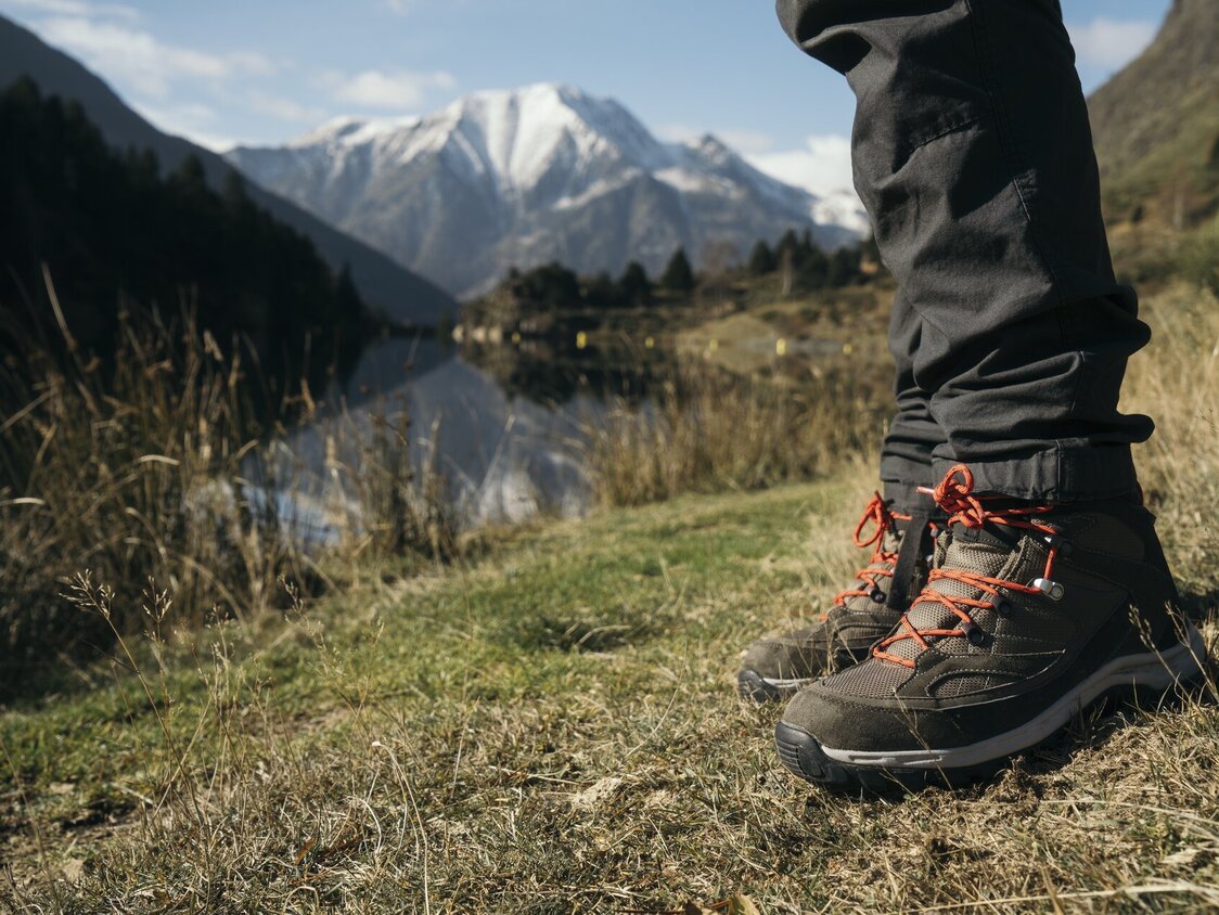 Man sieht die Wanderschuhe einer Person, die an einem Bergsee steht.