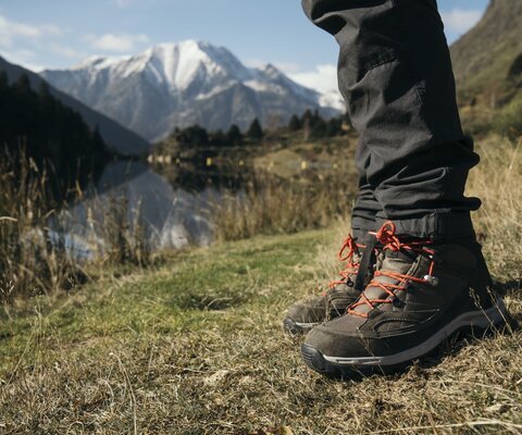 Man sieht die Wanderschuhe einer Person, die an einem Bergsee steht.