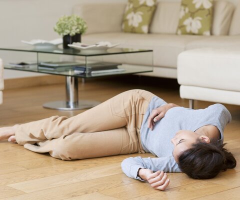 Frau liegt bewusstlos am Boden eines Wohnzimmers.