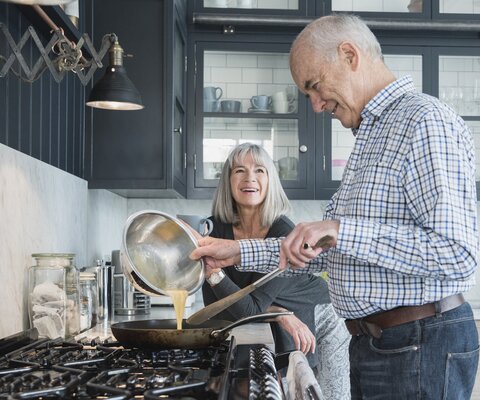 Älteres Ehepaar steht in der Küche und kocht gemeinsam.