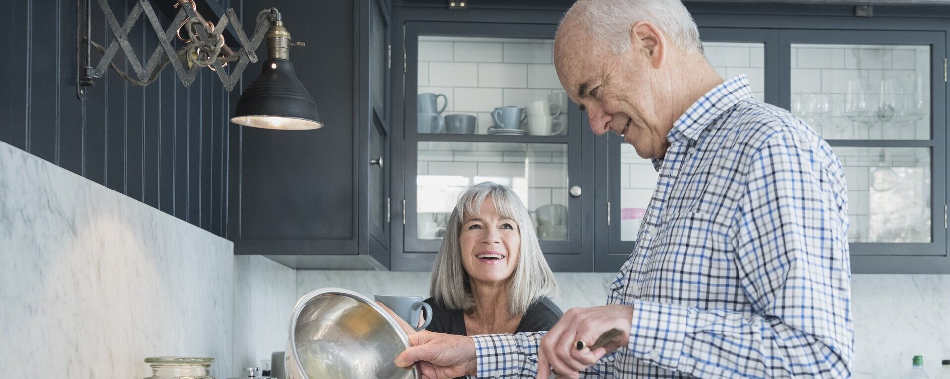 Ein alter Mann macht essen, während eine alte Frau zuguckt.