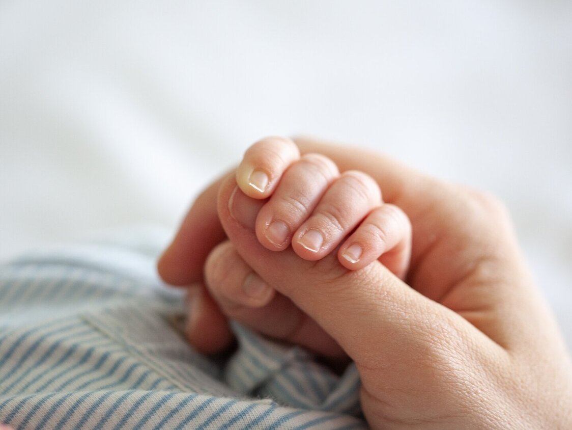 Ein Baby hält mit seiner Hand den Daumen eines Erwachsenen.