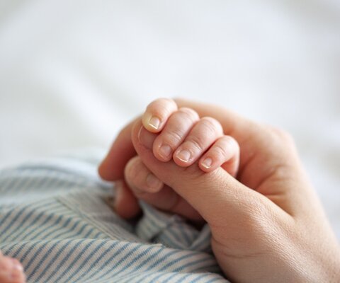 Ein Baby hält mit seiner Hand den Daumen eines Erwachsenen.