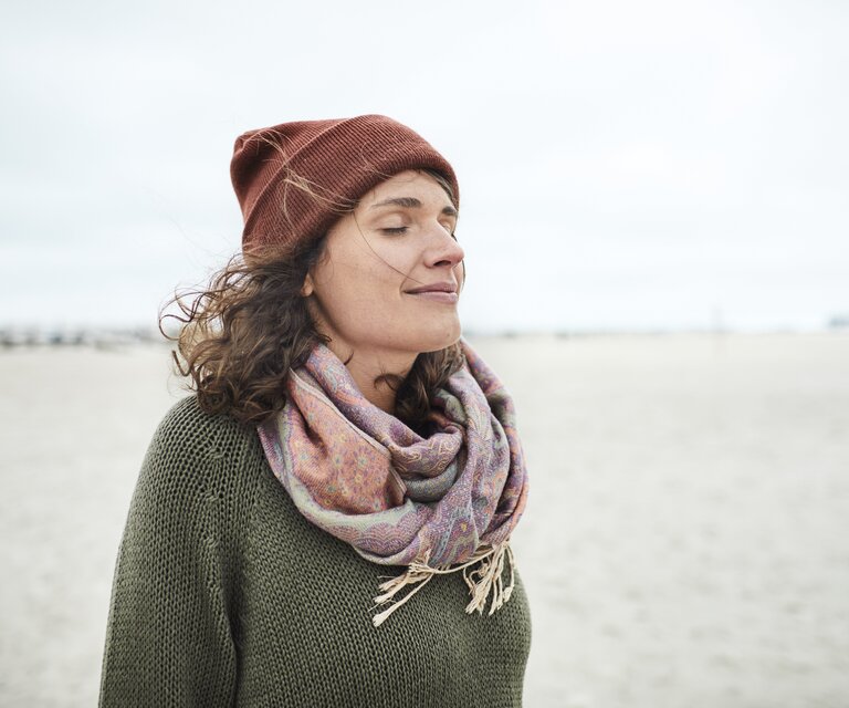 Portrait eine lächelnden Frau mit Mütze und Schal am Strand.