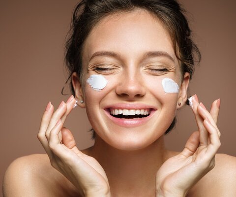 Das Foto zeigt das Gesicht einer Frau, die sich Creme auf die Wangen aufträgt.