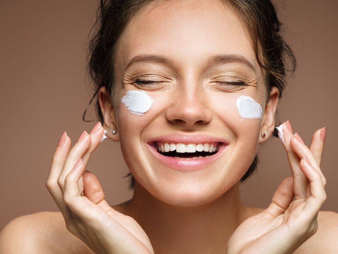 Das Foto zeigt das Gesicht einer Frau, die sich Creme auf die Wangen aufträgt.