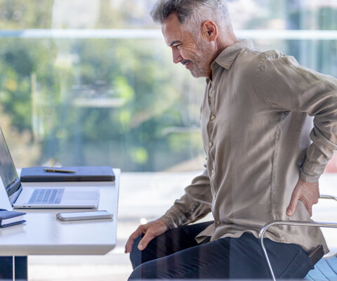 Reifer Geschäftsmann, der sich vor Schmerzen den Rücken zuhält.