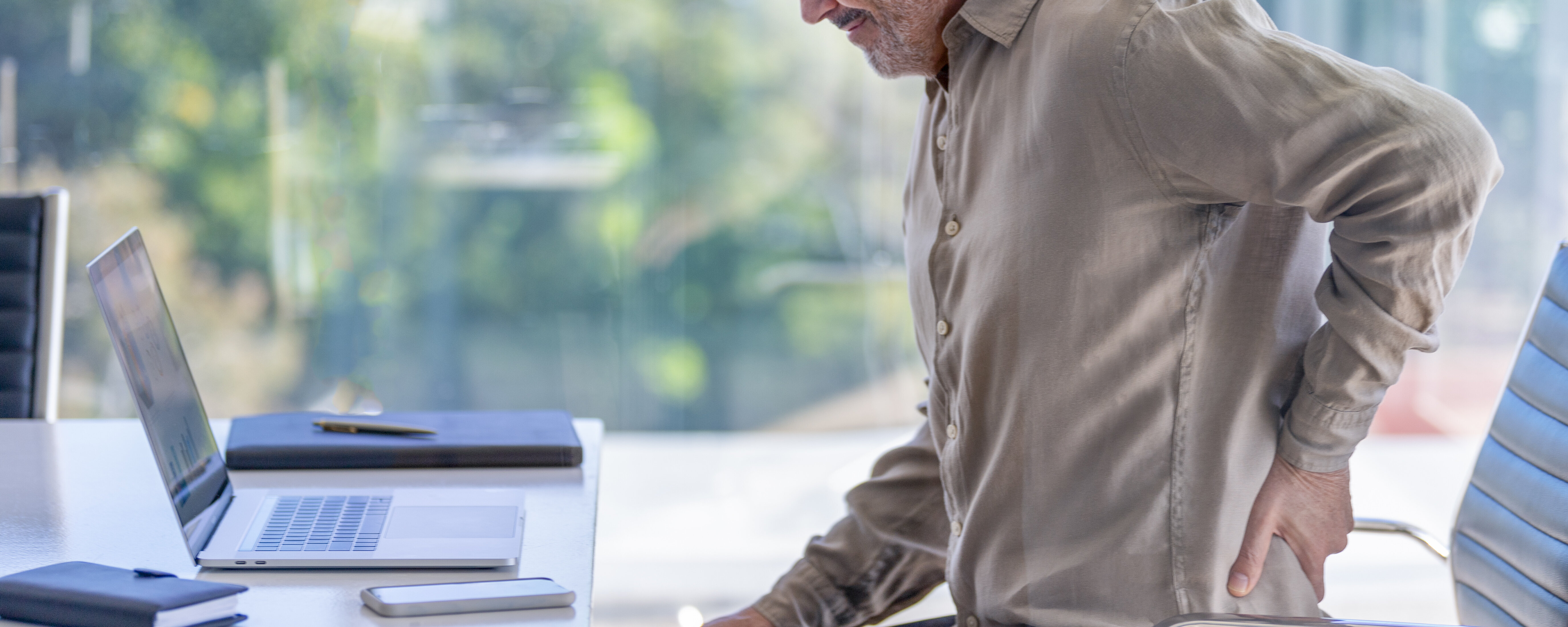Reifer Geschäftsmann, der sich vor Schmerzen den Rücken zuhält.