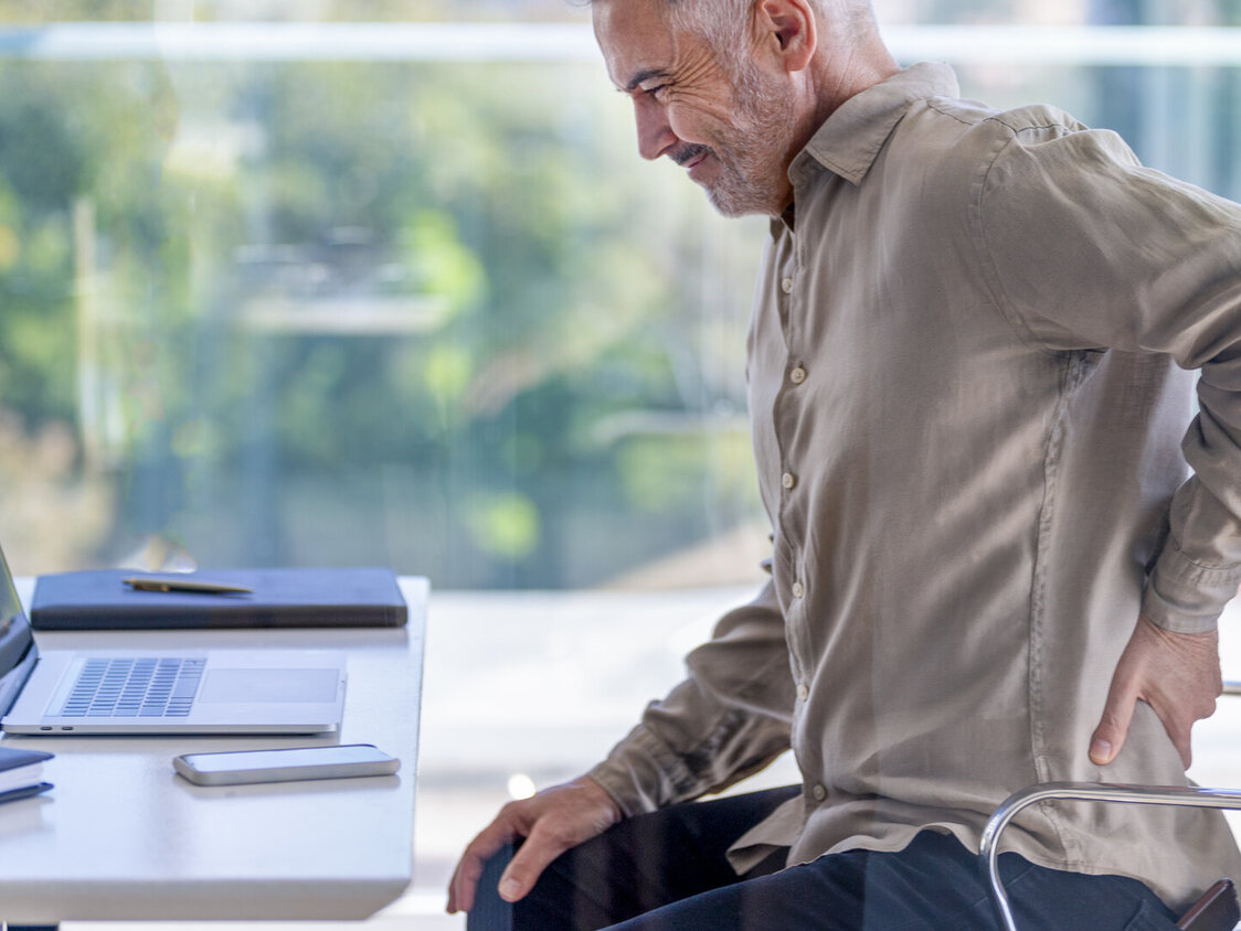 Reifer Geschäftsmann, der sich vor Schmerzen den Rücken zuhält.