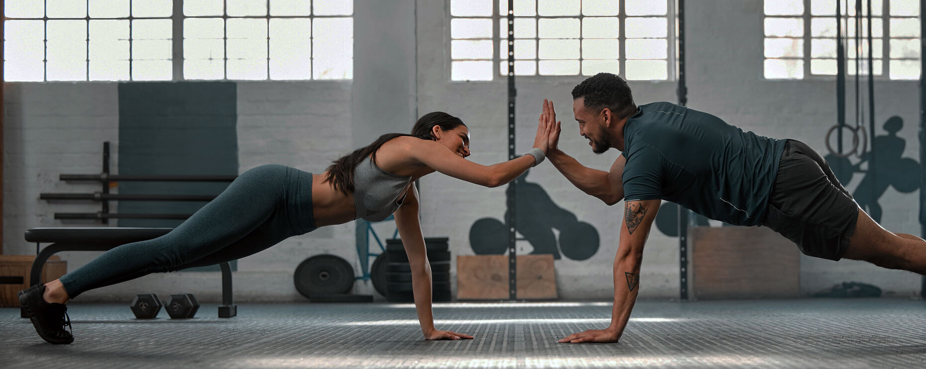 Fitness-Partner, die zusammen trainieren und Liegestütze machen, High Five im Fitnessstudio. Ein fitter und aktiver Mann und eine Frau trainieren in einer Gesundheitseinrichtung als Teil ihrer Trainingsroutine. Ein Paar bei einer Übung