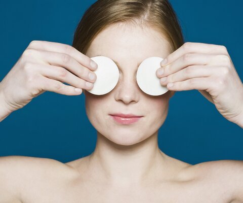 Eine Person legt sich zwei Wattepads auf die Augen.