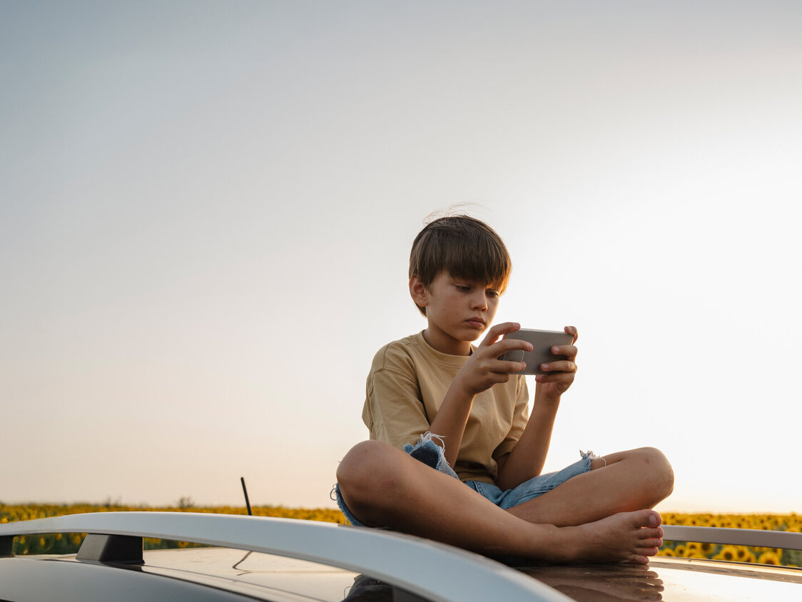 Kind sitzt und hält ein Smartphone in den Händen.