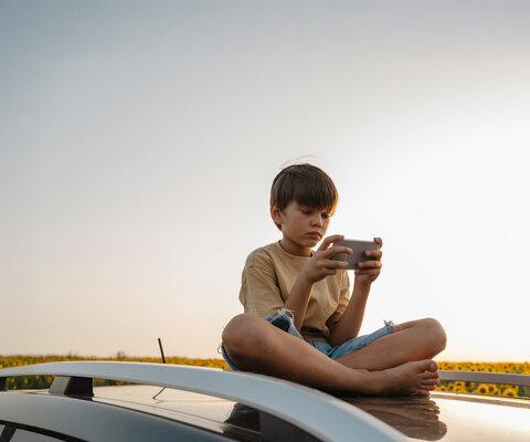 Kind sitzt und hält ein Smartphone in den Händen.