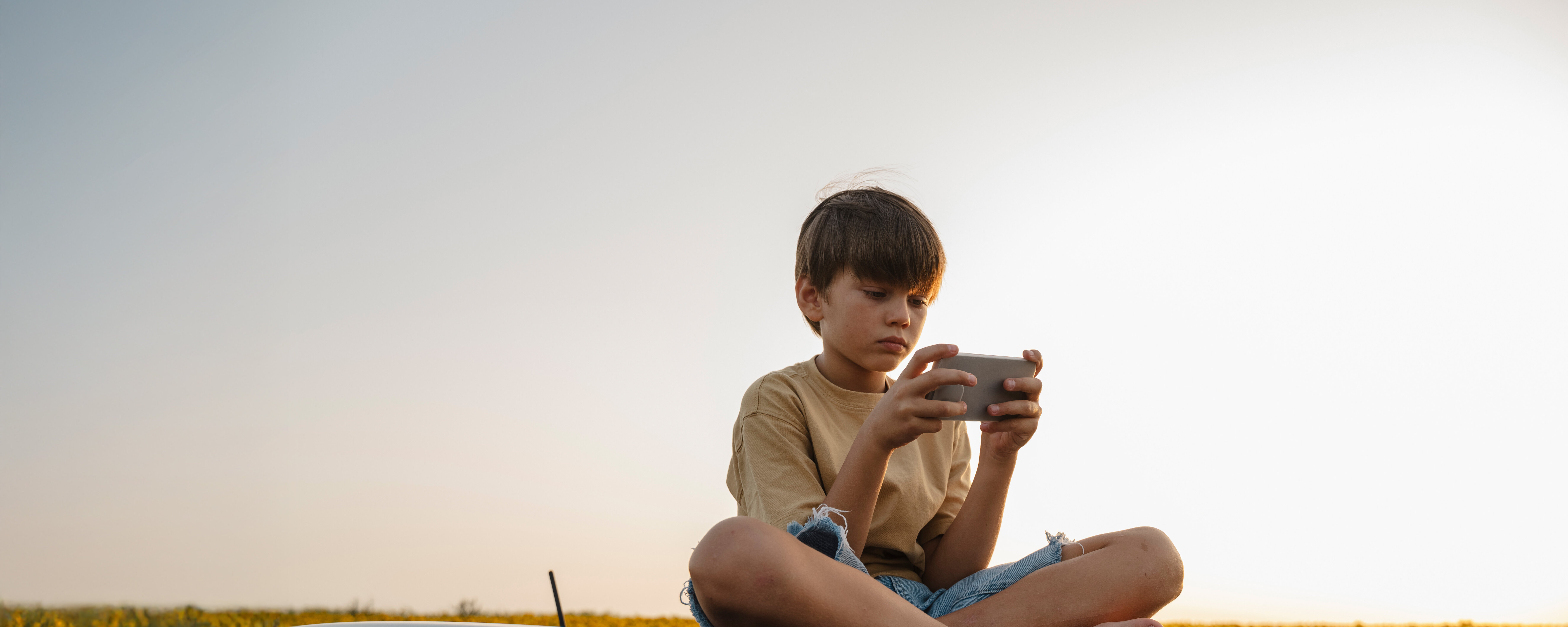 Kind sitzt und hält ein Smartphone in den Händen.