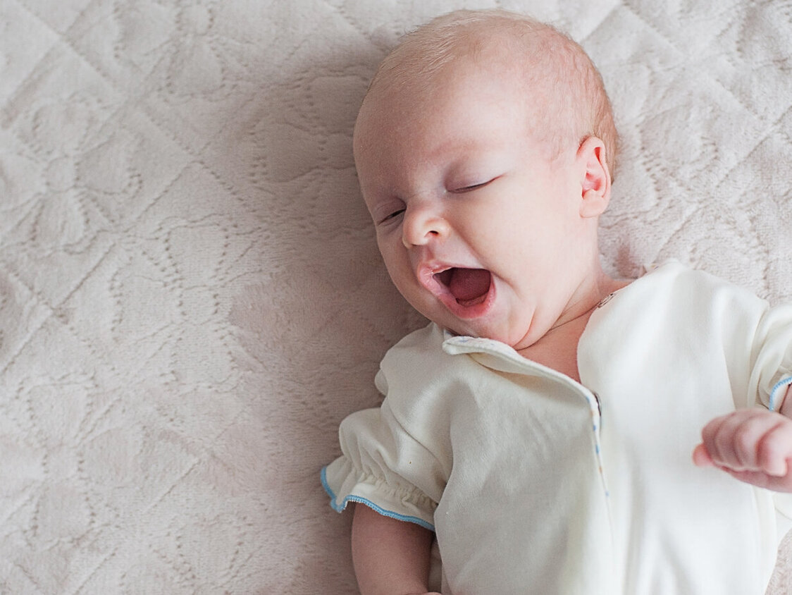 Ein gähnendes Baby liegt auf einer Decke