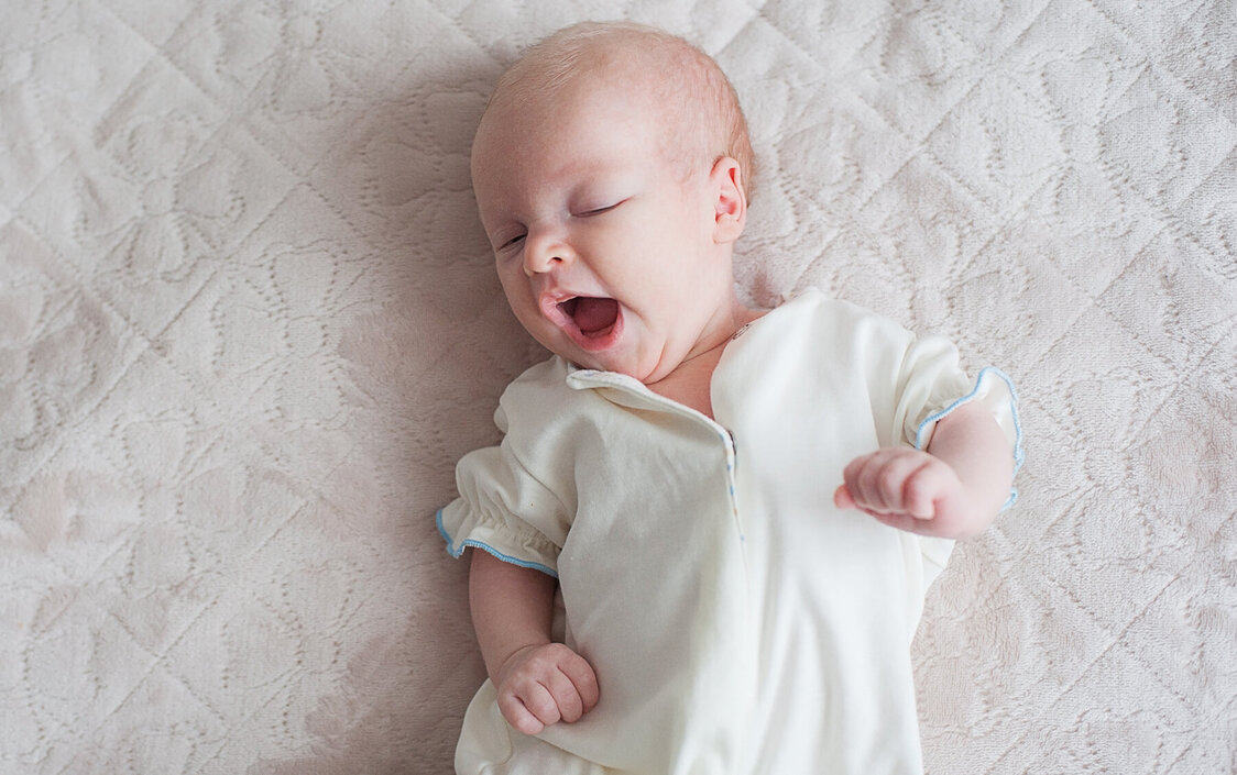 Ein gähnendes Baby liegt auf einer Decke