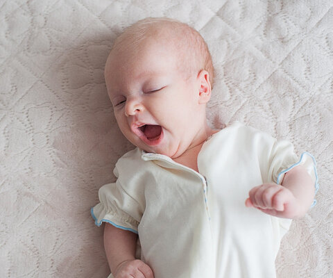 Ein gähnendes Baby liegt auf einer Decke