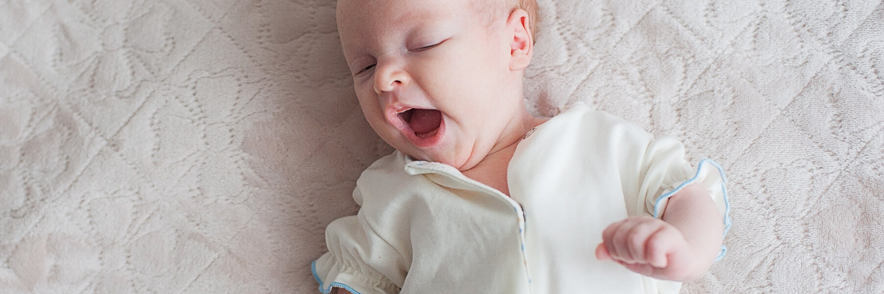 Ein gähnendes Baby liegt auf einer Decke