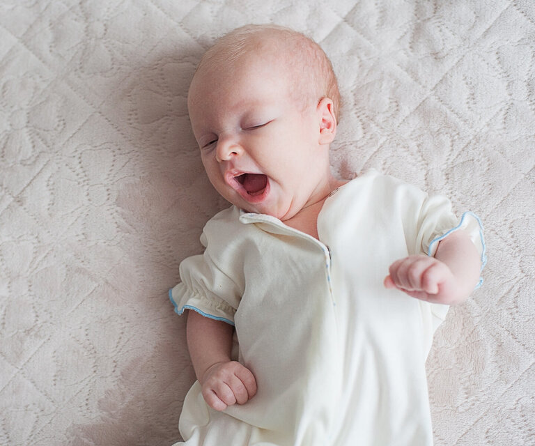 Ein gähnendes Baby liegt auf einer Decke