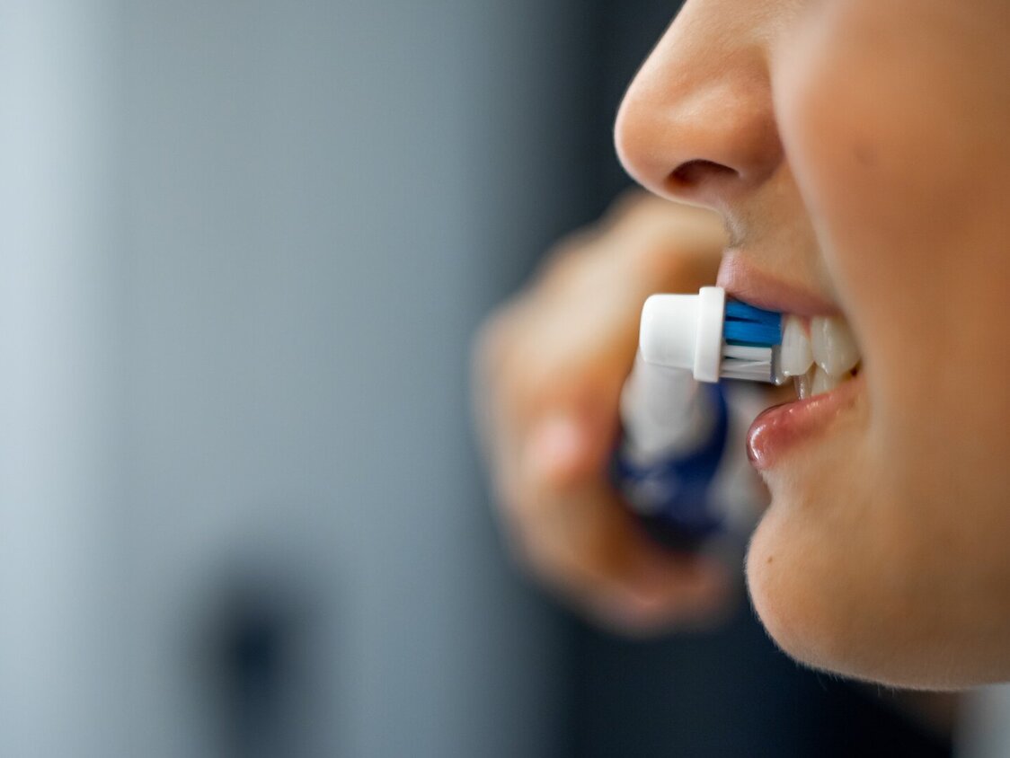 Nahaufnahme des Mundes eines Teenagers, der eine elektrische Zahnbürste in der Hand hält, lächelt und sich im Badezimmer die Zähne putzt.