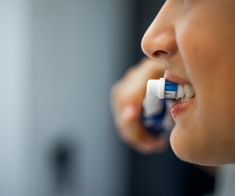 Nahaufnahme des Mundes eines Teenagers, der eine elektrische Zahnbürste in der Hand hält, lächelt und sich im Badezimmer die Zähne putzt.