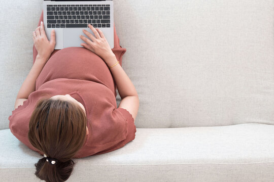  Eine schwangere Frau auf einem Sofa am Laptop sitzend.