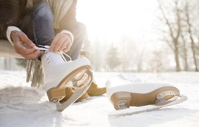 Frau sitzt auf einer Bank in einer Winterlandschaft und zieht Schlittschuhe an.