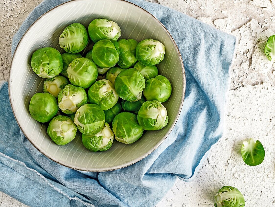 Auf einer Platte steht eine weiße Schüssel, die mit Rosenkohl gefüllt ist.