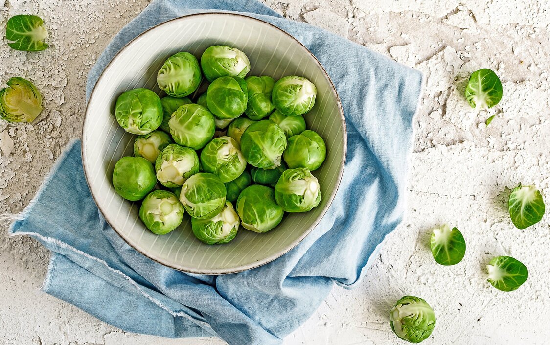 Auf einer Platte steht eine weiße Schüssel, die mit Rosenkohl gefüllt ist.