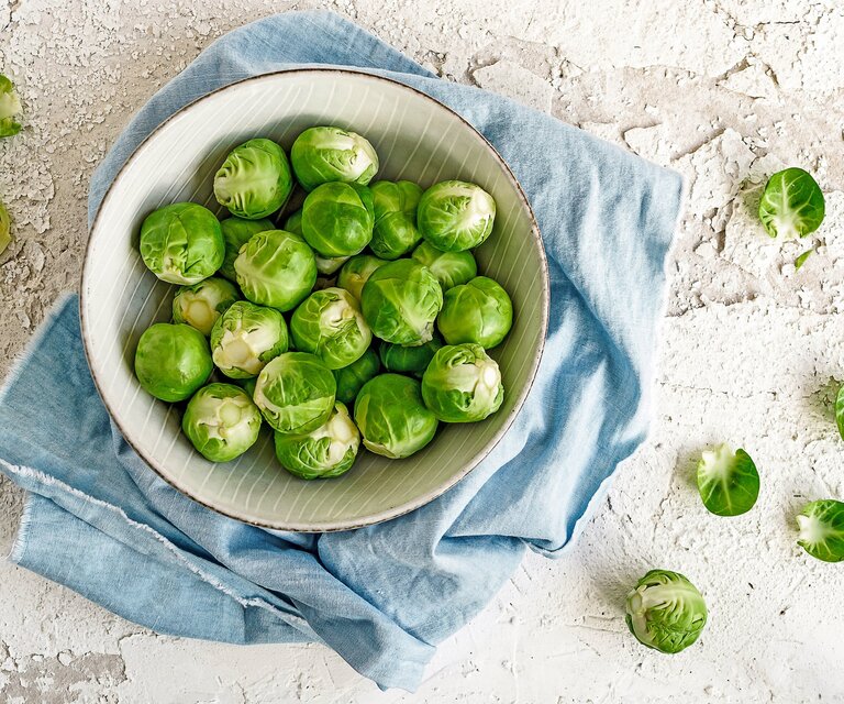 Auf einer Platte steht eine weiße Schüssel, die mit Rosenkohl gefüllt ist.