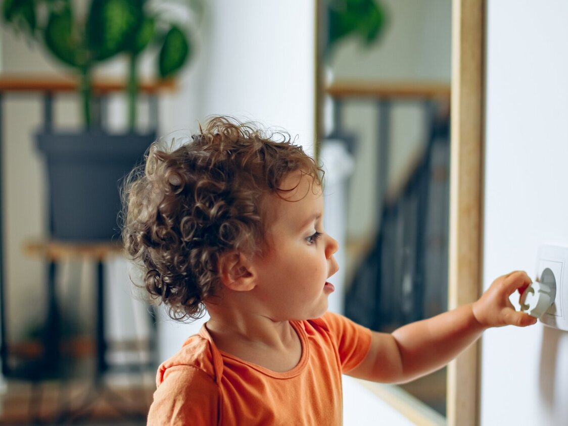 Kleinkind spielt mit Steckdose in der Wand.