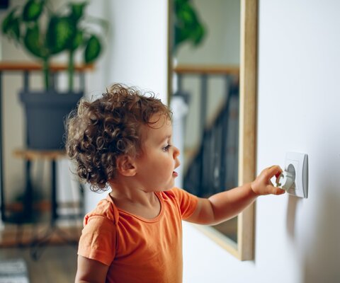 Kleinkind spielt mit Steckdose in der Wand.
