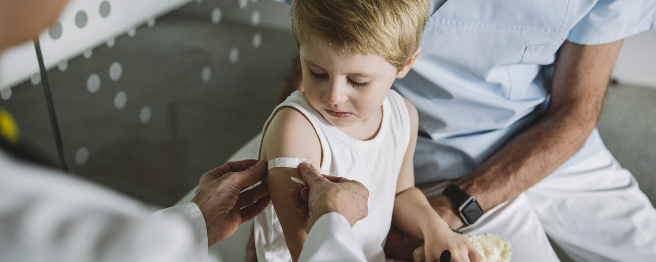 Kinderarzt klebt Pflaster auf den Arm eines Kleinkindes nach einer Impfung.
