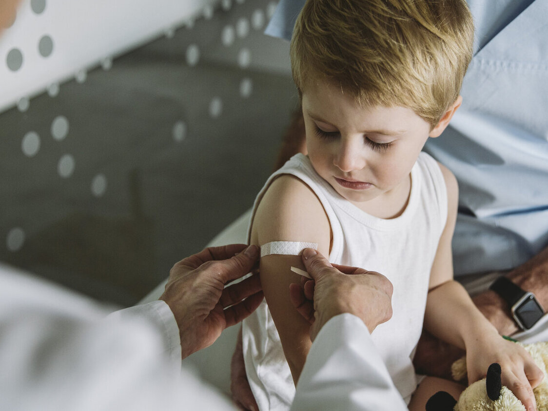 Kinderarzt klebt Pflaster auf den Arm eines Kleinkindes nach einer Impfung.