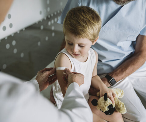 Kinderarzt klebt Pflaster auf den Arm eines Kleinkindes nach einer Impfung.