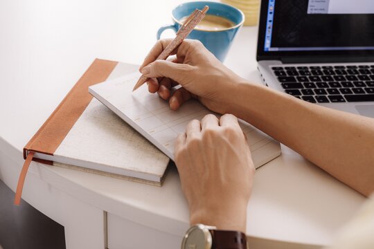 240809_artikelbild_notizen_block_organisieren_gettyimages_1214774789 An einem Tisch, macht sich jemand Notizen in einem Block.